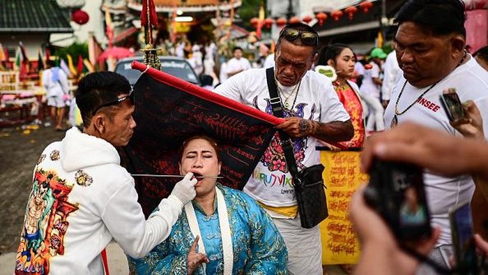 Super Ekstrem, Festival Vegetarian di Thailand Ini Bikin Ngilu A devotee of the Jor Soo Gong Naka shrine with a ship model pierced through his cheek waits to take part in a procession during the annual Vegetarian Festival in Phuket on September 27, 2022. - The festival, back after two years of hiatus because of the Covid-19 pandemic, features religious devotees who slash themselves with swords, pierce their cheeks with sharp objects and commit other painful acts to purify themselves, taking on the sins of the community. (Photo by MANAN VATSYAYANA / AFP) (Photo by MANAN VATSYAYANA/AFP via Getty Images)
