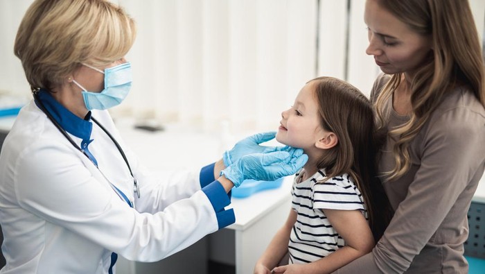 Concept of professional consultation in healthcare system. Pediatrician woman examining tonsils of smiling little girl in medical office