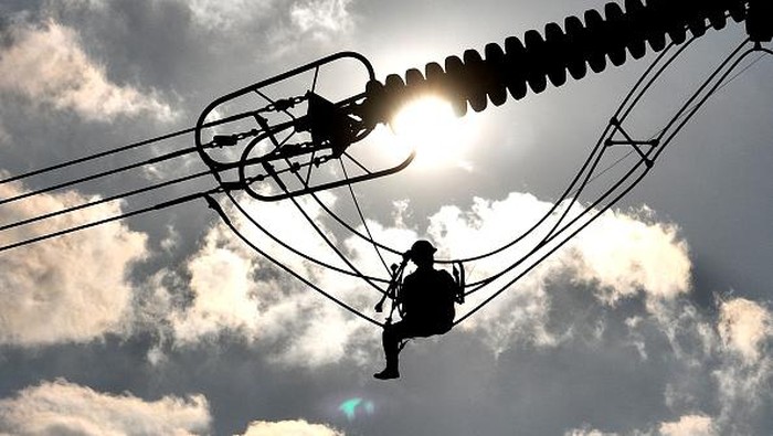 LIANYUNGANG, CHINA - SEPTEMBER 28: An electrician carries out maintenance work on electric wires of a 500KV transmission line project at sunset on September 28, 2022 in Lianyungang, Jiangsu Province of China. (Photo by Geng Yuhe/VCG via Getty Images)