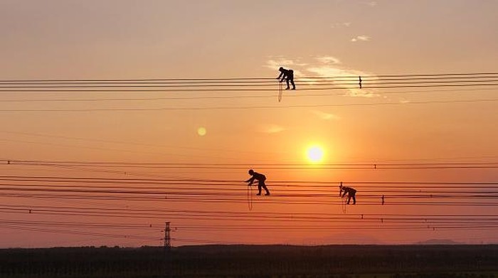 LIANYUNGANG, CHINA - SEPTEMBER 28: An electrician carries out maintenance work on electric wires of a 500KV transmission line project at sunset on September 28, 2022 in Lianyungang, Jiangsu Province of China. (Photo by Geng Yuhe/VCG via Getty Images)