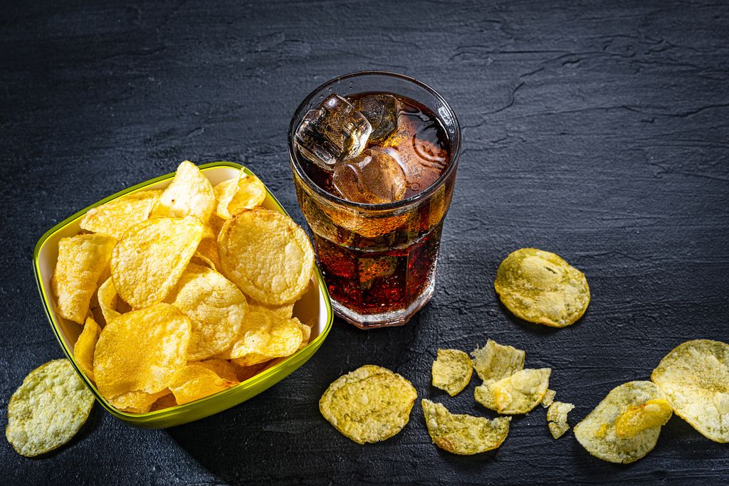 Unhealthy food: high angle view of a cola soda glass and potato chips in a bowl shot on black slate table. Predominant colors are yellow and black. High resolution 42Mp studio digital capture taken with Sony A7rII and Sony FE 90mm f2.8 macro G OSS lens