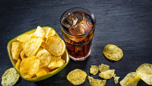 Unhealthy food: high angle view of a cola soda glass and potato chips in a bowl shot on black slate table. Predominant colors are yellow and black. High resolution 42Mp studio digital capture taken with Sony A7rII and Sony FE 90mm f2.8 macro G OSS lens