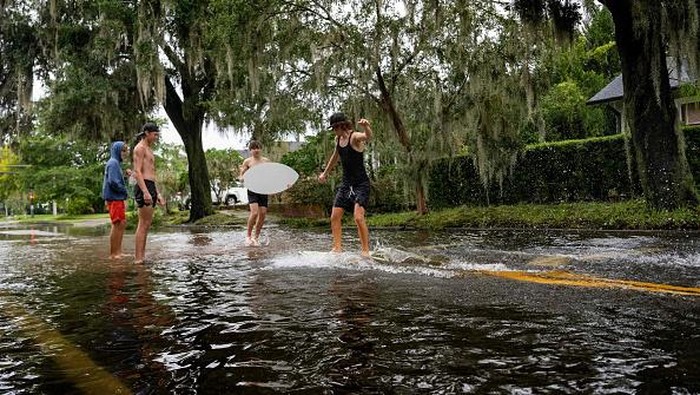 Warga Florida Asik Main Selancar di Tengah Banjir Boys skim board on a flooded street in the aftermath of Hurricane Ian in Orlando, Florida on September 29, 2022. - Hurricane Ian left much of coastal southwest Florida in darkness early on Thursday, bringing