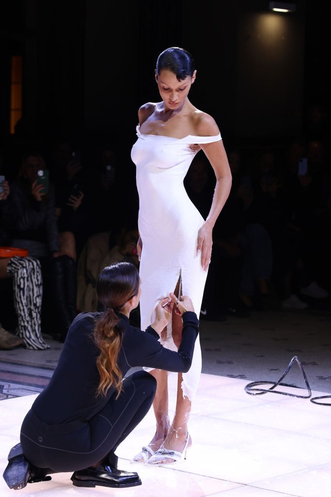 Seorang wanita tampak merobek dress Bella Hadid sehingga busana tersebut memiliki belahan di paha. Foto: Getty Images/Estrop