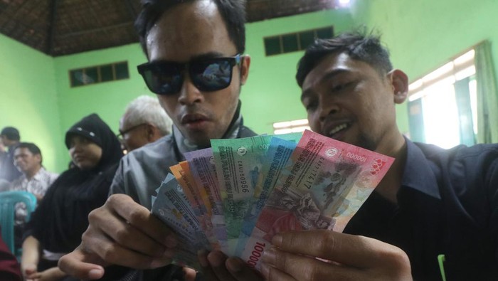 SOSIALISASI KEASLIAN UANG RUPIAH KEPADA TUNA NETRA Petugas membantu penyandang tuna netra meraba uang rupiah saat sosialisasi keaslian uang rupiah di Balai Desa Ngebrak, Kediri, Jawa Timur, Sabtu (1/10/2022). Bank Indonesia kantor perwakilan Kediri melakukan sosialisasi ciri-ciri keaslian uang rupiah tahun emisi 2022 kepada difabel hingga tingkat desa. ANTARA FOTO/Prasetia Fauzani/YU