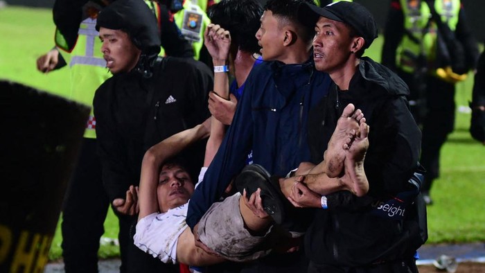 Aksi Solidaritas Suporter di Tengah Kerusuhan Maut Kanjuruhan In this picture taken on October 1, 2022, a group of people carry a man after a football match between Arema FC and Persebaya Surabaya at Kanjuruhan stadium in Malang, East Java. - At least 127 people died at a football stadium in Indonesia late on October 1 when fans invaded the pitch and police responded with tear gas, triggering a stampede, officials said. (Photo by AFP) (Photo by STR/AFP via Getty Images)