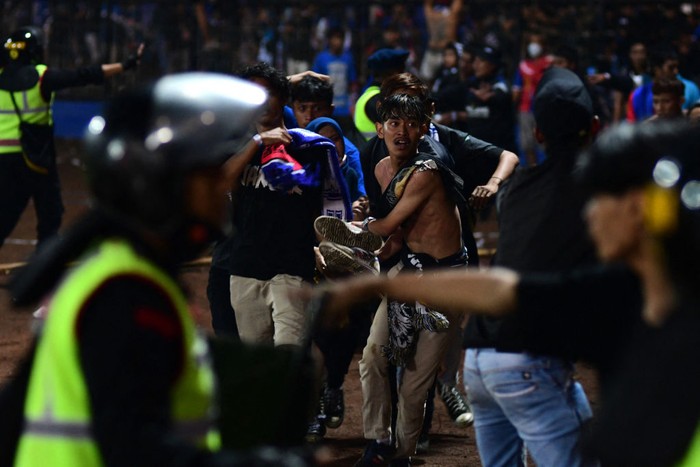 In this picture taken on October 1, 2022, a group of people carry a man after a football match between Arema FC and Persebaya Surabaya at Kanjuruhan stadium in Malang, East Java. - At least 127 people died at a football stadium in Indonesia late on October 1 when fans invaded the pitch and police responded with tear gas, triggering a stampede, officials said. (Photo by AFP) (Photo by STR/AFP via Getty Images)