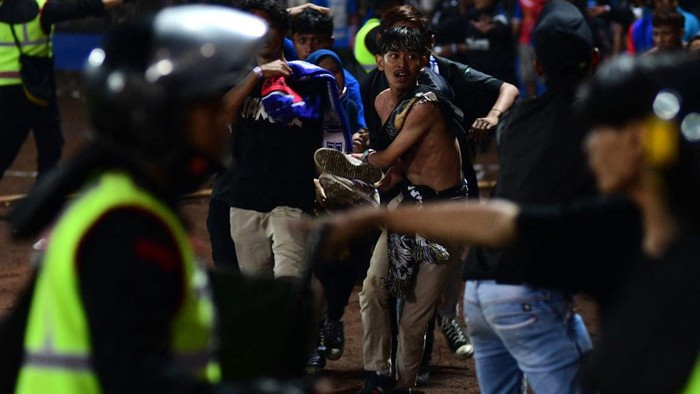 In this picture taken on October 1, 2022, a group of people carry a man after a football match between Arema FC and Persebaya Surabaya at Kanjuruhan stadium in Malang, East Java. - At least 127 people died at a football stadium in Indonesia late on October 1 when fans invaded the pitch and police responded with tear gas, triggering a stampede, officials said. (Photo by AFP) (Photo by STR/AFP via Getty Images)