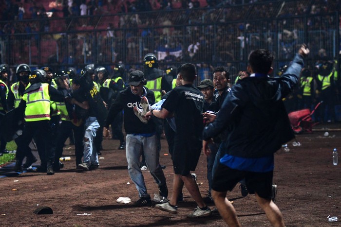 In this picture taken on October 1, 2022, a group of people carry a man after a football match between Arema FC and Persebaya Surabaya at Kanjuruhan stadium in Malang, East Java. - At least 127 people died at a football stadium in Indonesia late on October 1 when fans invaded the pitch and police responded with tear gas, triggering a stampede, officials said. (Photo by AFP) (Photo by STR/AFP via Getty Images)