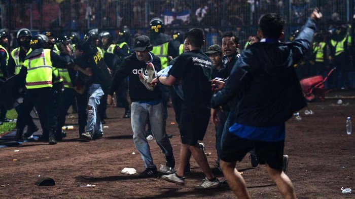 Aksi Solidaritas Suporter di Tengah Kerusuhan Maut Kanjuruhan In this picture taken on October 1, 2022, a group of people carry a man after a football match between Arema FC and Persebaya Surabaya at Kanjuruhan stadium in Malang, East Java. - At least 127 people died at a football stadium in Indonesia late on October 1 when fans invaded the pitch and police responded with tear gas, triggering a stampede, officials said. (Photo by AFP) (Photo by STR/AFP via Getty Images)