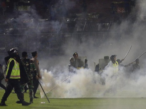 Police officers and soldiers stand amid tear gas smoke after clashes between fans during a soccer match at Kanjuruhan Stadium in Malang, East Java, Indonesia, Saturday, Oct. 1, 2022. Panic following police actions left over 100 dead, mostly trampled to death, police said Sunday. (AP Photo/Yudha Prabowo)