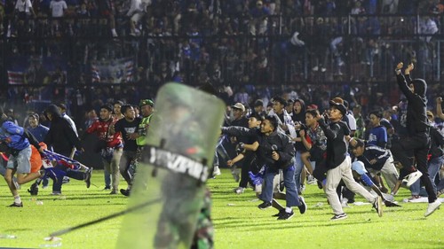 Police officers and soldiers stand amid tear gas smoke after clashes between fans during a soccer match at Kanjuruhan Stadium in Malang, East Java, Indonesia, Saturday, Oct. 1, 2022. Panic following police actions left over 100 dead, mostly trampled to death, police said Sunday. (AP Photo/Yudha Prabowo)