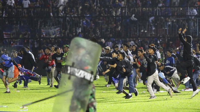 Foto-foto Kerusuhan di Stadion Kanjuruhan, 127 Orang Tewas Police officers and soldiers stand amid tear gas smoke after clashes between fans during a soccer match at Kanjuruhan Stadium in Malang, East Java, Indonesia, Saturday, Oct. 1, 2022. Panic following police actions left over 100 dead, mostly trampled to death, police said Sunday. (AP Photo/Yudha Prabowo)