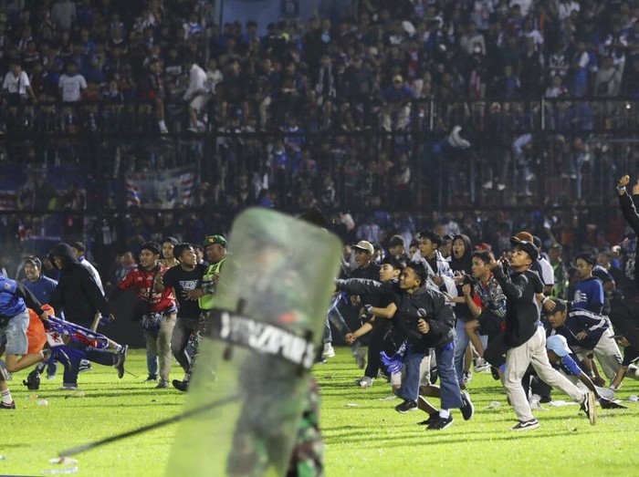 Police officers and soldiers stand amid tear gas smoke after clashes between fans during a soccer match at Kanjuruhan Stadium in Malang, East Java, Indonesia, Saturday, Oct. 1, 2022. Panic following police actions left over 100 dead, mostly trampled to death, police said Sunday. (AP Photo/Yudha Prabowo)