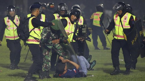 Police officers and soldiers stand amid tear gas smoke after clashes between fans during a soccer match at Kanjuruhan Stadium in Malang, East Java, Indonesia, Saturday, Oct. 1, 2022. Panic following police actions left over 100 dead, mostly trampled to death, police said Sunday. (AP Photo/Yudha Prabowo)