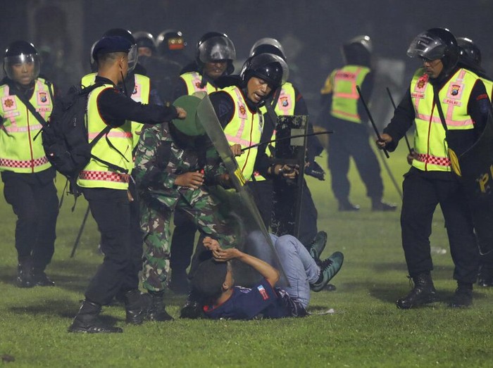 Police officers and soldiers stand amid tear gas smoke after clashes between fans during a soccer match at Kanjuruhan Stadium in Malang, East Java, Indonesia, Saturday, Oct. 1, 2022. Panic following police actions left over 100 dead, mostly trampled to death, police said Sunday. (AP Photo/Yudha Prabowo)