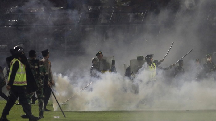 Police officers and soldiers stand amid tear gas smoke after clashes between fans during a soccer match at Kanjuruhan Stadium in Malang, East Java, Indonesia, Saturday, Oct. 1, 2022. Panic following police actions left over 100 dead, mostly trampled to death, police said Sunday. (AP Photo/Yudha Prabowo)