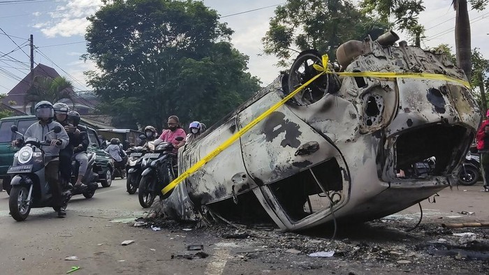 Motorists ride past the wreckage of a car burned during a clash between supporters of two soccer teams, outside Kanjuruhan Stadium in Malang, East Java, Indonesia, Sunday, Oct. 2, 2022. Panic following police actions at the stadium left over 100 dead, mostly trampled to death, police said Sunday. (AP Photo/Hendra Permana)