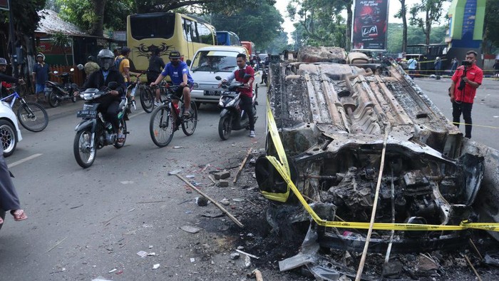Warga Lalu Lalang di Dekat Mobil yang Terbakar Usai Tragedi Kanjuruhan MALANG, INDONESIA - OCTOBER 2: People pass by a damaged police vehicle outside Kanjuruhan stadium in Malang, East Java, Indonesia, on 02 October 2022. At least 127 people including police officers were killed mostly in stampedes after a clash between fans of two Indonesian soccer teams, according to the police. (Photo by Aman Rochman/Anadolu Agency via Getty Images)