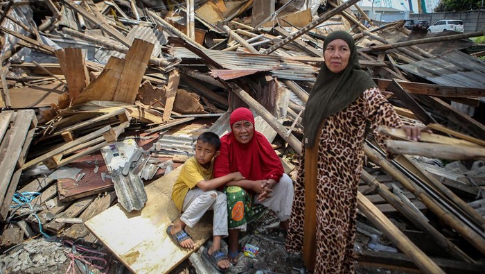 Warga duduk di atas reruntuhan bangunan yang hampir rata dengan tanah.