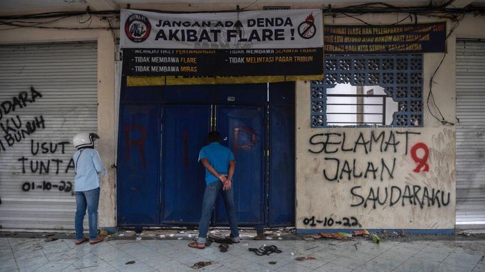 Warga melihat kondisi Stadion Kanjuruhan dari balik pintu. Terlihat dinding Stadion yang dicoret untuk mengungkapkan rasa belasungkawa dengan bertuliskan Selamat Jalan Saudaraku.