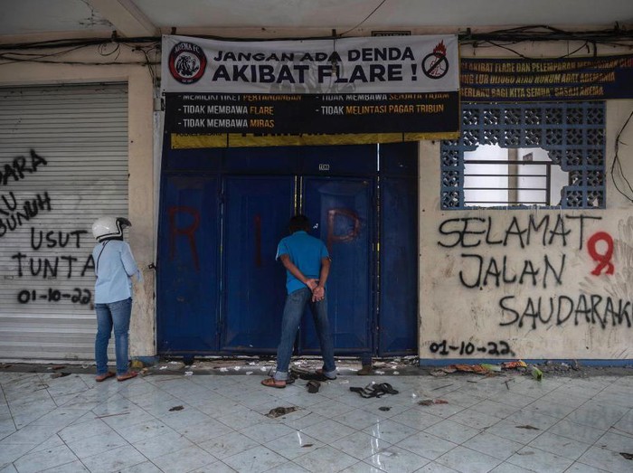 Warga melihat kondisi Stadion Kanjuruhan dari balik pintu. Terlihat dinding Stadion yang dicoret untuk mengungkapkan rasa belasungkawa dengan bertuliskan Selamat Jalan Saudaraku.
