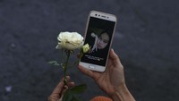 Seorang warga memegang bunga di samping foto korban kerusuhan di Stadion Kanjuruhan, Malang, jawa Timur, Minggu (2/10/2022). ANTARA FOTO/Zabur Karuru.