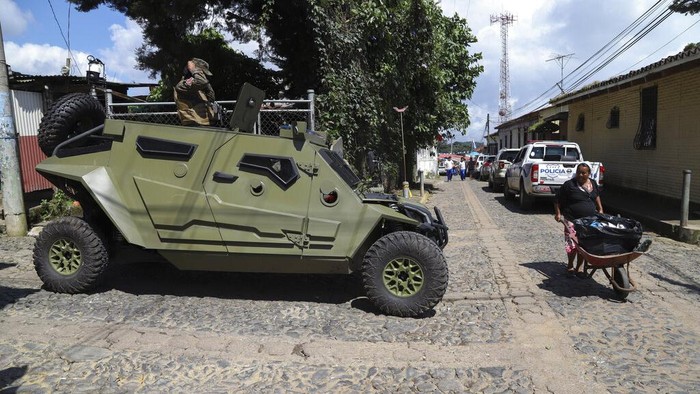 Basmi Geng Jalanan, Ribuan Tentara Kepung Kota di El Salvador Seorang wanita berjalan di depan mobil lapis baja tentara saat tentara berpatroli di jalan-jalan kota Comasagua, El Salvador, Senin (3/10/2022) waktu setempat.