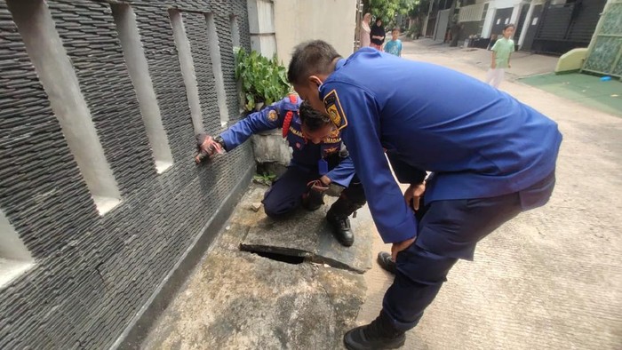 Dua petugas damkar Cibinong Bogor mendatangi rumah warga usai menerima laporan seekor anak kucing terjebak dalam selokan seharian.