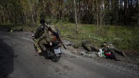 Prajurit Ukraina mengendarai sepeda motor melewati mayat prajurit Rusia di kota Lyman, Ukraina, Senin (3/10/2022) waktu setempat.  