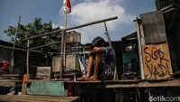 Seorang anak duduk termenung di gubuk rumahnya dengan latar belakang bendera merah putih.