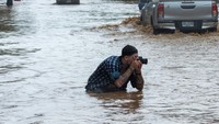 Seorang jurnalis foto asing mengambil gambar di tengah banjir.