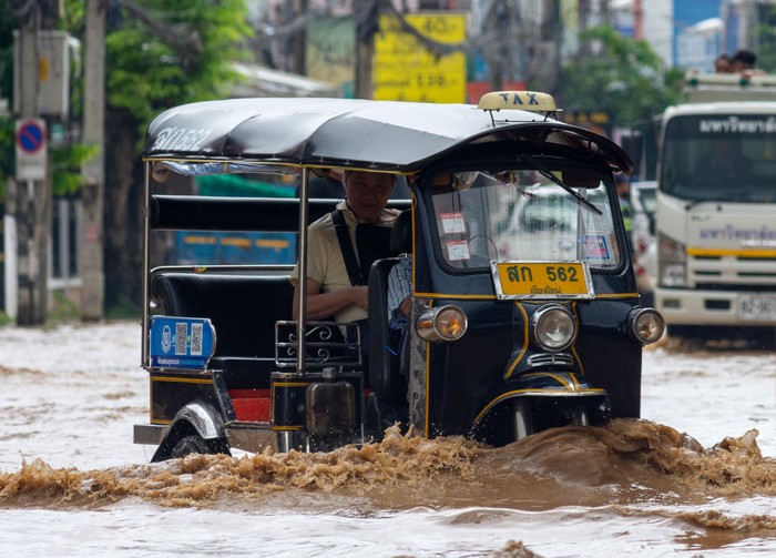 Pengemudi tuk tuk membawa penumpang melewati banjir.