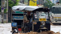 Pengemudi tuk tuk membawa penumpang melewati banjir.