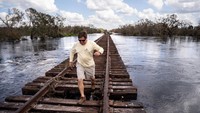Mack Martin berjalan di sepanjang rel kereta api yang dikelilingi oleh air banjir di Peace River.