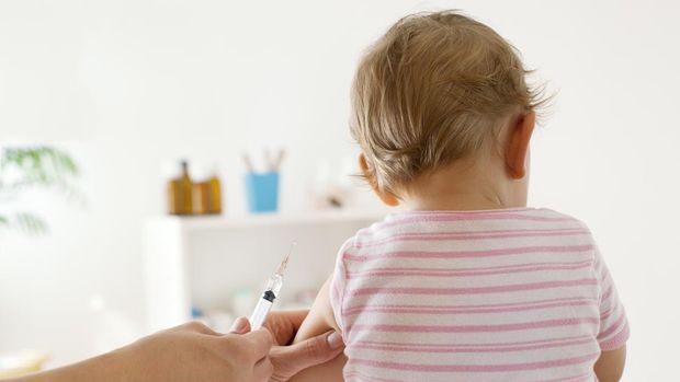 Bck View of baby girl patient receiving vaccine at the doctor's office, focus on hand holding vaccine