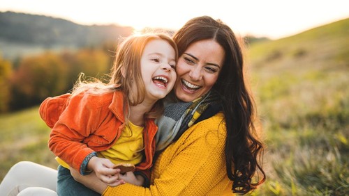 A portrait of young mother with a small daughter sitting on a ground in autumn nature at sunset.