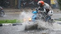 Seorang pemotor menerobos genangan.