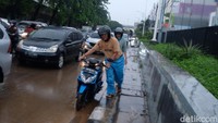 Cuaca masih hujan. Salah seorang warga tampak mendorong motor yang mogok. 