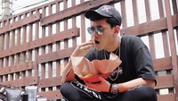 Indra Kenz juga tak segan makan nasi bungkus nih! Ia asyik menikmati makanan sederhana ini sambil duduk bersila.