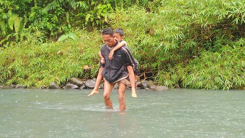 Ketua Tempek 1 Banjar Nusamara Dewa Komang Putra Wiarsana (44), mengendong anaknya yang pulang sekolah melintasi sungai, Kamis sore (6/10/2022)
