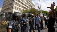 Seorang pengunjuk rasa meneriakkan slogan-slogan menentang ketika polisi anti huru hara Lebanon berjaga di depan gedung bank sentral, tempat para demonstran anti-pemerintah berunjuk rasa menentang Gubernur Bank Sentral Lebanon Riad Salameh. AP/Hassan Ammar