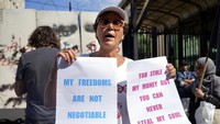 Seorang pengunjuk rasa dari kelompok aktivis Depositors Outcry memegang plakat saat dia berdiri di depan gedung bank sentral, di mana demonstran anti-pemerintah berunjuk rasa menentang Gubernur Bank Sentral Lebanon Riad Salameh dan krisis keuangan yang semakin dalam, di Beirut, Lebanon. AP/Bilal Hussein