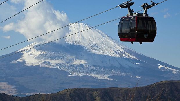 Kereta gantung melintas di depan Gunung Fuji, Hakone, Jepang. Jika cuaca sedang bagus, travelers bisa melihat panorama Gunung Fuji yang tertutup salju dari kejauhan. Indah kan? (John S Lander/Getty Images)