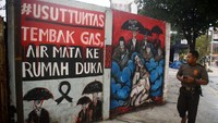 Seorang polisi berjalan di sebelah mural yang menggambarkan orang terinjak-injak hingga menyebabkan 131 orang tewas, di sebelahnya grafiti bertuliskan Selidiki secara menyeluruh, menembakkan gas air mata menyebabkan kematian,. Insiden ini menjadi salah satu bencana paling mematikan dalam sejarah sepak bola Tanah Air. Putri/AFP/Getty Images