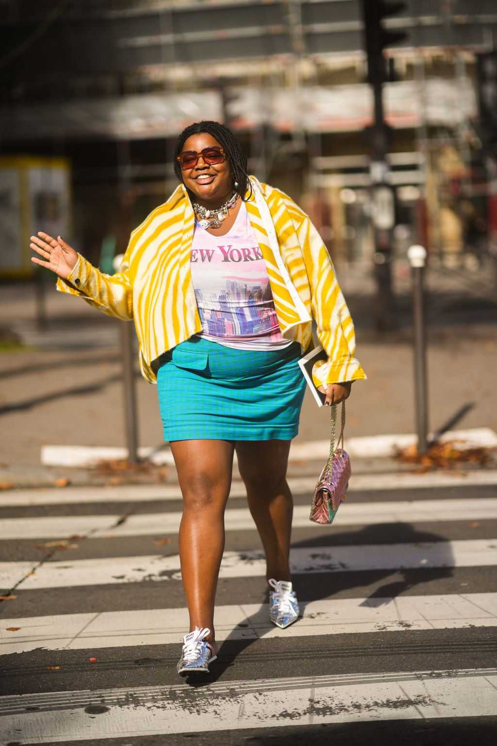 PARIS, FRANCE - OCTOBER 05: Gabriella Karefa-Johnson wears sunglasses, large silver chain pendant necklace, a white / purple / pink tied and dye with New York city print pattern t-shirt, a white and yellow zebra print pattern jacket, a blue and green checkered pattern short skirt, a blue and pink shiny leather 2.55 handbag from Chanel, silver leather pointed sneakers from Miu Miu, outside Miu Miu, during Paris Fashion Week - Womenswear Spring Summer 2022, on October 05, 2021 in Paris, France. (Photo by Edward Berthelot/Getty Images)
