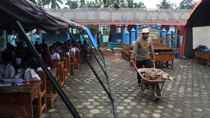 Atap SDN Gelang 7 Ambruk, Siswa Belajar di Tenda Darurat Sejumlah siswa belajar di tenda darurat di samping petugas yang membawa material atap sekolah yang ambruk di SDN Gelang 7, Desa Gelang, Sumberbaru, Jember, Jawa Timur, Senin (10/10/2022). Sebanyak 175 siswa terpaksa belajar di tenda darurat karena atap sekolah ambruk setelah diguyur hujan deras pada Sabtu (8/10).