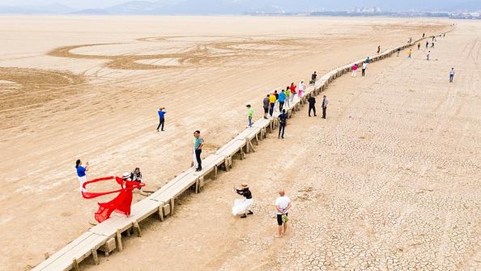 Jembatan Batu Berusia 400 Tahun Muncul di Tengah Danau Kering China JIUJIANG, CHINA : People walk on an ancient stone bridge which emerges from dried Poyang Lake on 2022 in Jiujiang, Jiangxi Province of China. Poyang Lake shrinks by about 70 percent due to persistent drought. (Photo by Li Jie/VCG via Getty Images)