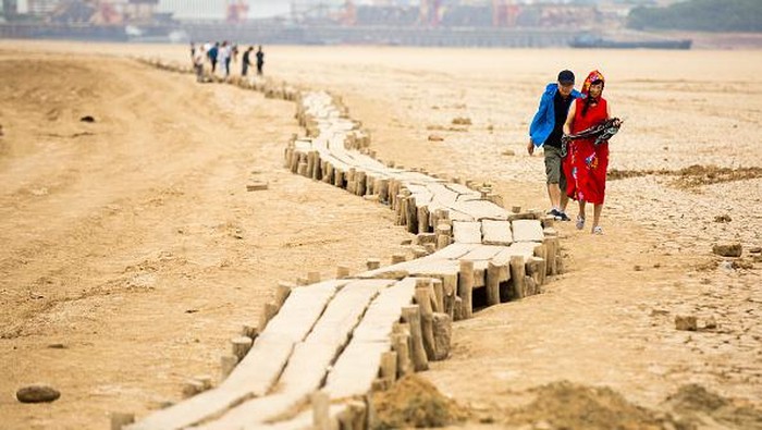 Jembatan Batu Berusia 400 Tahun Muncul di Tengah Danau Kering China JIUJIANG, CHINA : People walk on an ancient stone bridge which emerges from dried Poyang Lake on 2022 in Jiujiang, Jiangxi Province of China. Poyang Lake shrinks by about 70 percent due to persistent drought. (Photo by Li Jie/VCG via Getty Images)