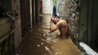 Warga yang bertahan di rumahnya memanfaatkan air banjir untuk mandi.